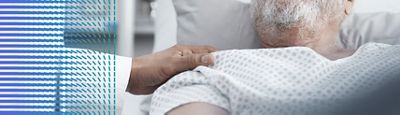 A clinician places their hand on a patient's shoulder while resting in a Hillrom hospital bed.