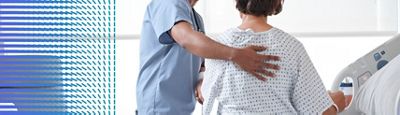 A clinician supports a patient's back while the patient sits upright in a Hillrom hospital bed.