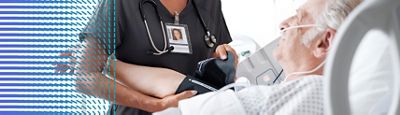 A clinician takes a patient's blood pressure while the patient rests in a hospital bed.