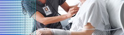 A clinician listens to a patient's heart while the patient sits upright in a Hillrom hospital bed.
