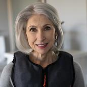 A woman with gray hair wears a fashionable, black Monarch® System vest with orange accents.