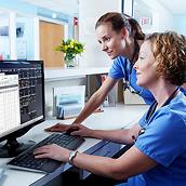 Zwei Pflegekräfte in einem Stationszimmer überprüfen über die Software der Connex Zentralstation auf einem Desktop-Computer den Patientenstatus