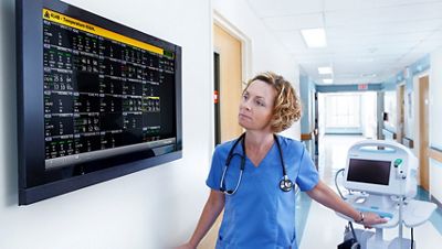Nurse views vital signs from the Connex Clinical Surveillance System in a hospital hallway, near a Connex Vital Signs Monitor