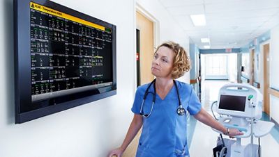 Nurse views vital signs from the Connex Clinical Surveillance System in a hospital hallway, near a Connex Vital Signs Monitor
