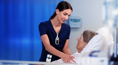 Clinician wearing a Voalte Linq device talks to patient in hospital bed 