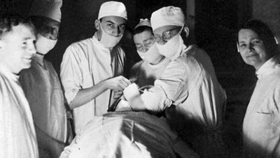 Surgeons work beneath a large, domed surgical light