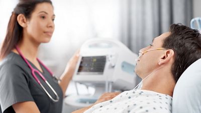 A clinician checks on her patient, wearing a nasal cannula, and reviews his vitals on the Connex...