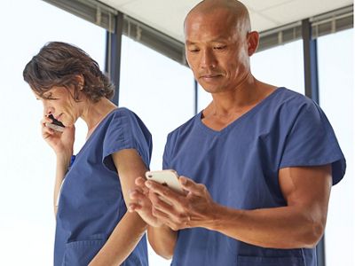 One nurse is talking on her phone and one nurse is texting on his phone after receiving patient information via Voalte Nurse Call. 