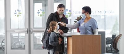 Receptionist screening child’s forehead with CareTemp thermometer