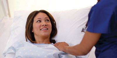 A patient lying in a Hillrom bed smiling at a caregiver.