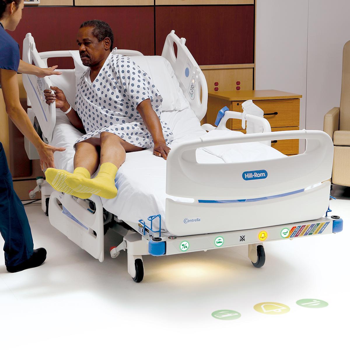 Female hospital clinician helps male patient exit the Centrella Smart+ Bed