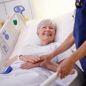 ผู้ป่วยหญิงสูงอายุหัวเราะกับผู้ดูแลขณะนอนอยู่บนเตียง Centrella Smart+ Bed