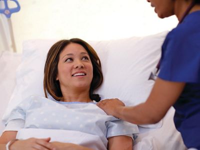 A patient lying in a Hillrom bed smiling at a caregiver.