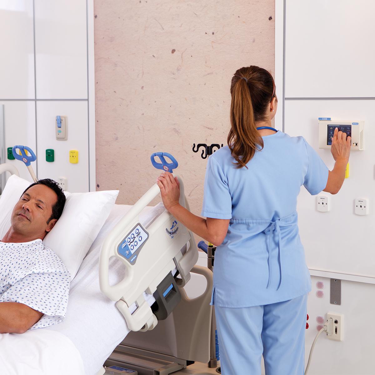 Sjuksköterska som interagerar med en väggmonterad skärm bredvid en patient
