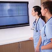 Två sjuksköterskor tittar på en stor väggmonterad skärm