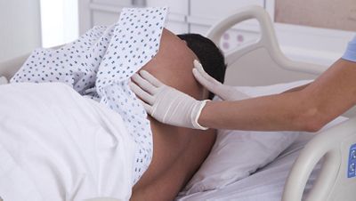 A gloved clinician performs a skin check on a patient’s back