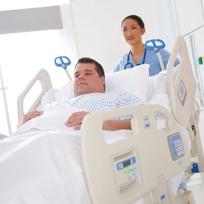 A relaxed caregiver does not strain as she pushes a Compella Bariatric Bed, in which a patient appears to recline comfortably.