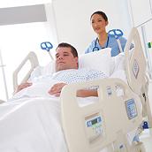 Un'operatrice sanitaria rilassata non compie alcuno sforzo mentre spinge un letto bariatrico Compella su cui è comodamente sdraiato un paziente.