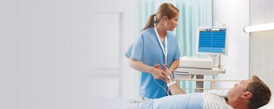 Patient in einem Krankenhausbett, der an das Welch Allyn® ELI® 380 EKG angeschlossen ist, während ein Arzt eine EKG-Ableitung anlegt.