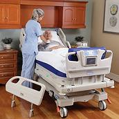 An over-the-shoulder view of a healthcare provider checking on her smiling patient as he recovers in an Envella therapy bed.