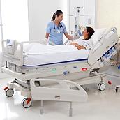 A hospital nurse speaks with her recovering wound care patient, who is lying in an Envella bed. The bed's siderails are down.