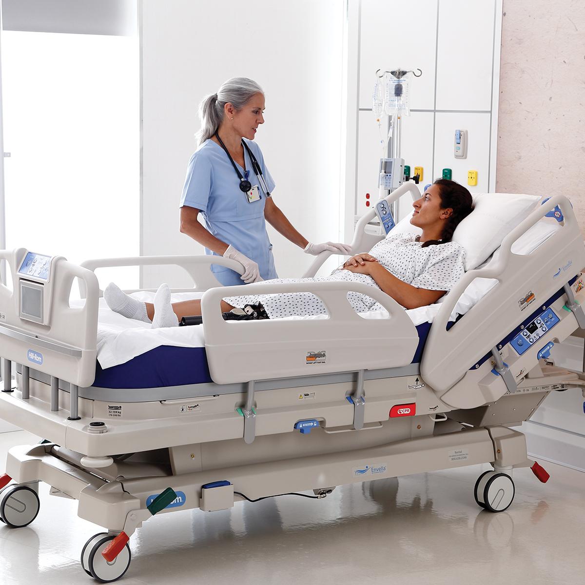 A clinician checks on her patient, who is recovering in an Envella therapy bed in a clean hospital room.