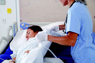 A nurse uses a positioning sheet to help her turn a patient in bed