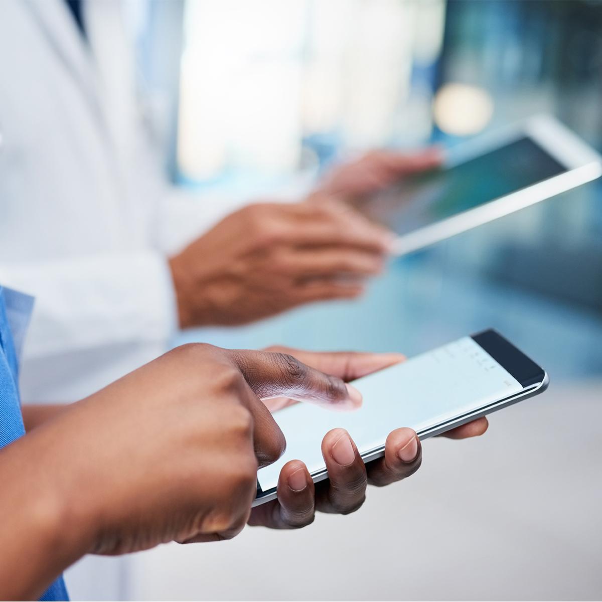 A clinician in blue scrubs and a physician in a lab coat send and receive information on their smartphones