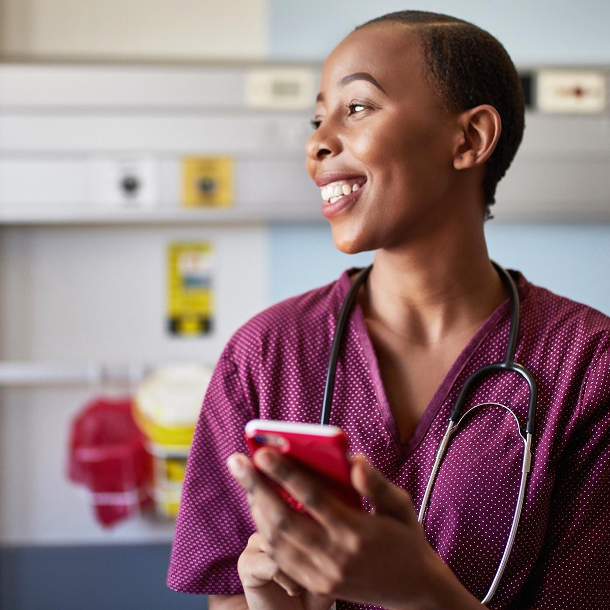 En sjuksköterska med en smarttelefon och en patient i bakgrunden
