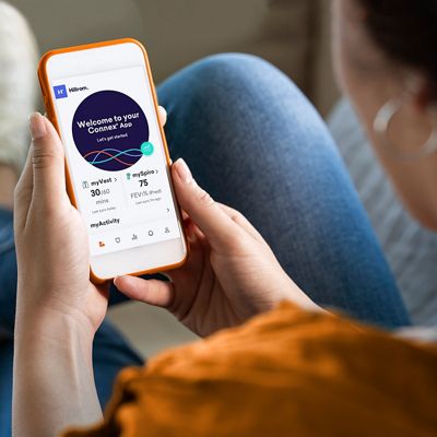 A woman relaxes on her couch while looking at the Hillrom Connex app on her iPhone.