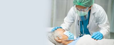 A doctor wearing gloves, surgical mask and face shield checks on an elderly patient in a hospital setting