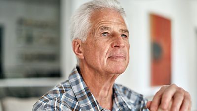 Male patient with a cane is sitting on a couch in his home. He looks confident knowing that his care team is monitoring his vitals while he remains at home.