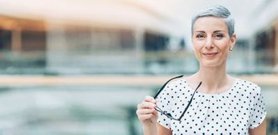 Eine professionelle Frau mit kurzen grauen Haaren lächelt selbstbewusst in die Kamera