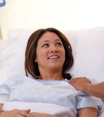 A patient lying in a Hillrom bed smiling at a caregiver