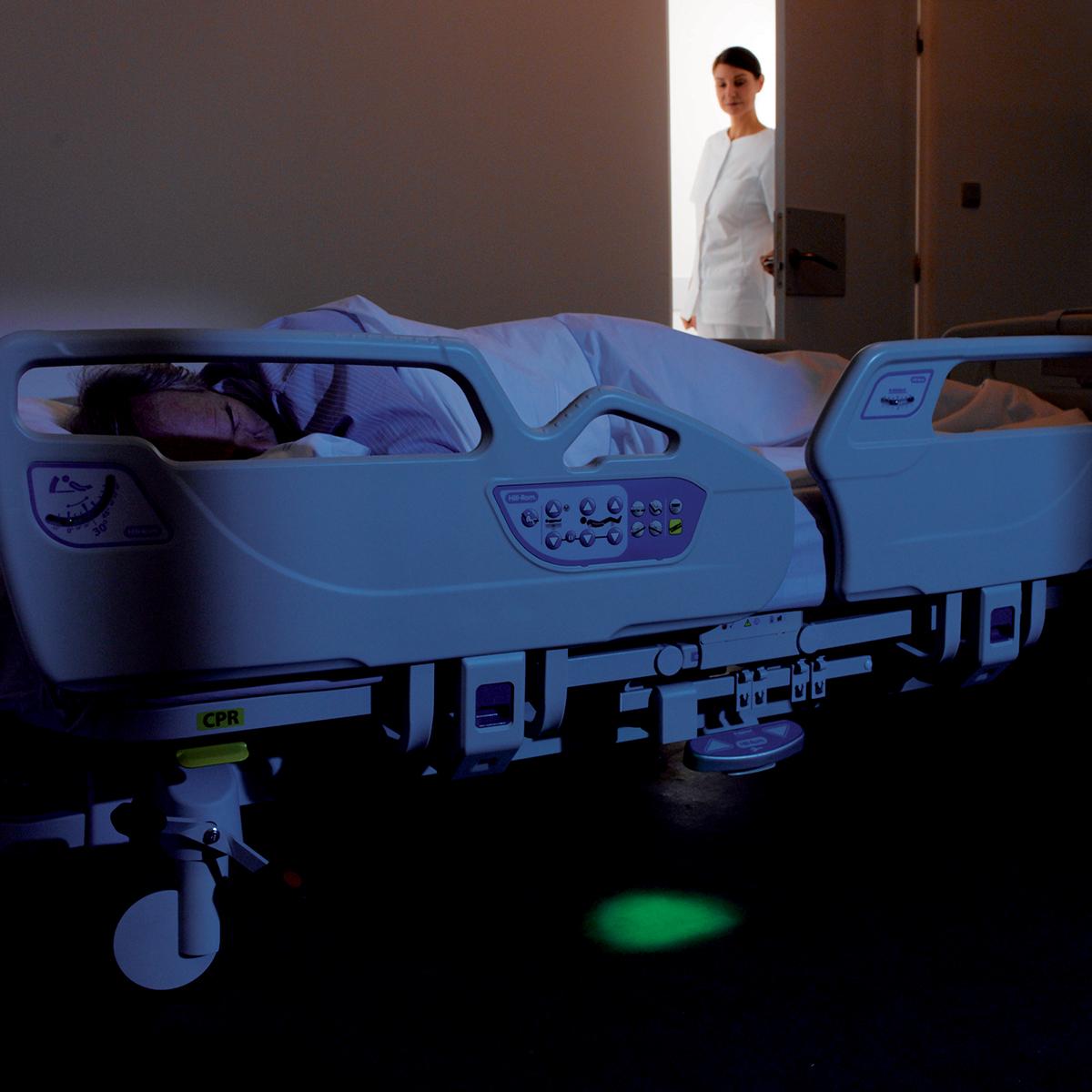A patient lies on his side in a Hillrom 900 bed, clinician in the background 