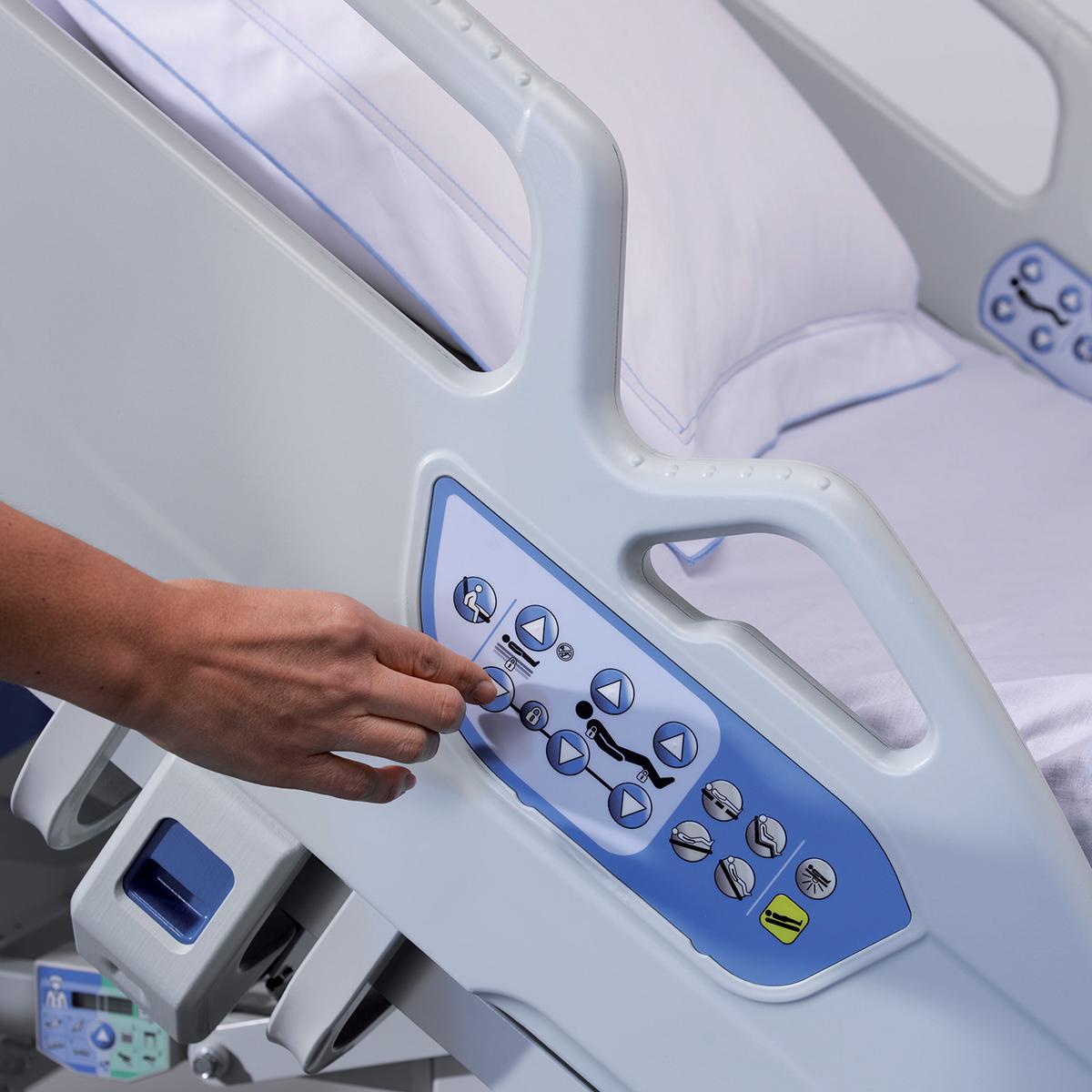 A hand presses a button on the Hillrom 900 bed’s control panel 