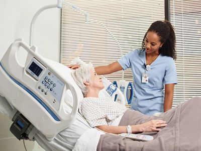 Caregiver wearing Hillrom Precision Locating staff badge attends to a patient in bed. 