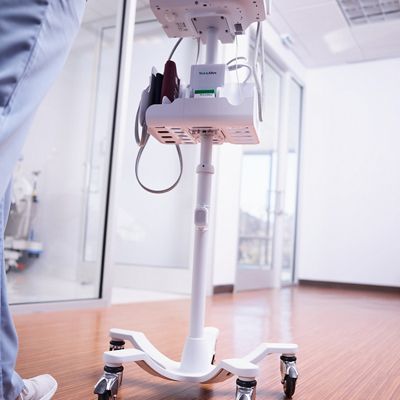 Caregiver walks down the hall with a piece of equipment tagged with Hillrom Precision Locating asset tag.