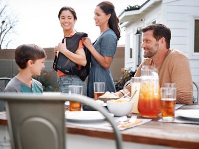  A family dines outside while a mother helps her daughter put on her Monarch Airway Clearance System