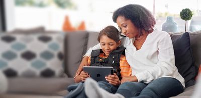 A mother and child relax on the couch at home. The child is receiving respiratory therapy with a Hillrom device.