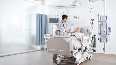 A clinician places his hand on the shoulder of a patient in an ICU bed