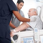 Two clinicians attending to an older patient sitting up in a hospital bed