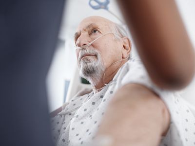 A clinician supports a patient’s back as he sits up in a Progressa+ ICU bed