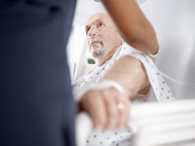 A clinician supports a patient back while he sits up in bed