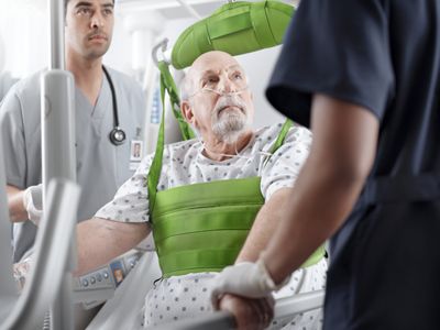 Two clinicians help a patient stand using a ceiling lift