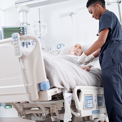 Female clinician tends to the IV of a male patient in a Progressa Bed