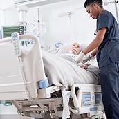 プログレッサベッドシステムに横たわる男性患者の IV を操作する女性医師