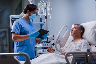 A clinician holding a tablet talks with a patient in a Progressa+ ICU bed