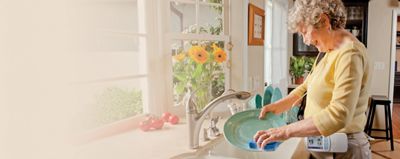A woman laughs and washes dishes at her kitchen sink while using the Life2000 Ventilation System