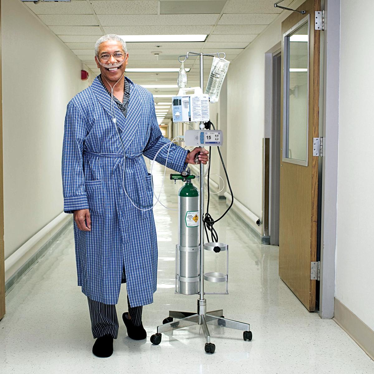 Smiling respiratory patient wearing nasal canula and walking in hospital hallway with Life2000 Ventilator and oxygen tank.